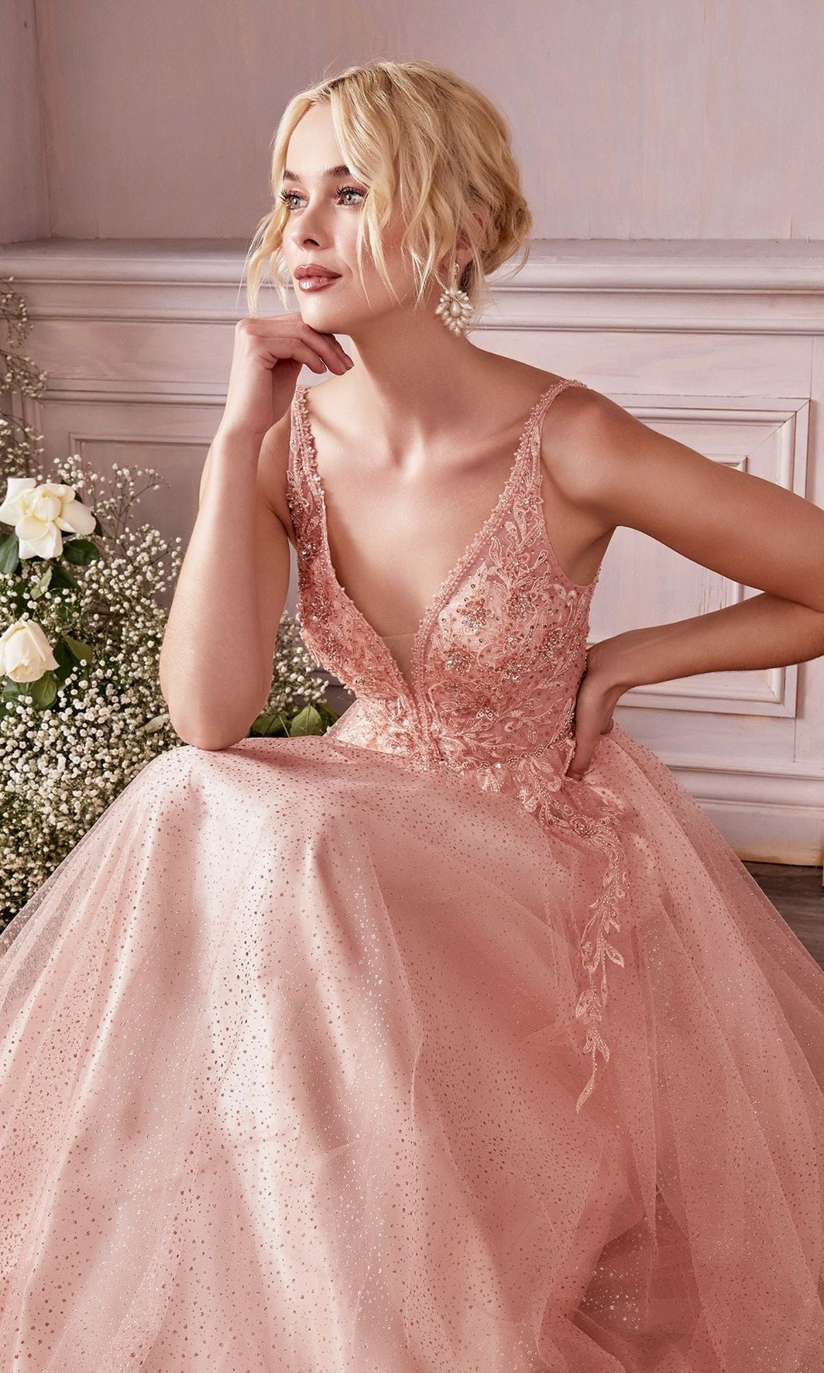 A woman in the Beaded-Bodice Long Pastel A-Line Prom Dress CD0196, featuring a sleeveless light pink beaded bodice with lace details, sits indoors beside a bouquet of white roses and baby's breath.